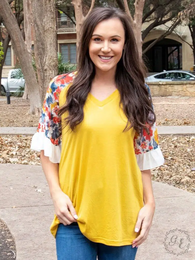 Smiling teenage girl wearing a mustard yellow, flowy shirt with vibrant floral 3/4 in sleeves